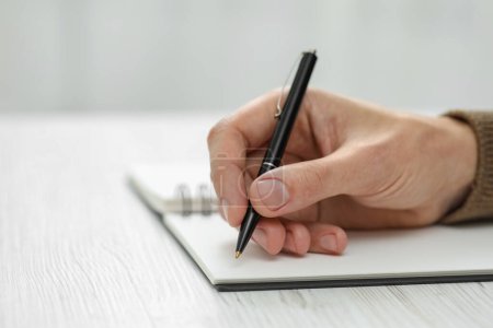 Téléchargez les photos : Man writing in notebook at white wooden table, closeup. Space for text - en image libre de droit