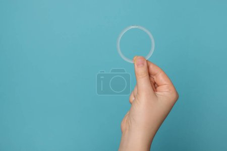 Téléchargez les photos : Woman holding diaphragm vaginal contraceptive ring on light blue background, closeup. Space for text - en image libre de droit