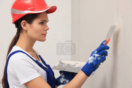 Photo for Professional worker in hard hat plastering wall with putty knives indoors - Royalty Free Image