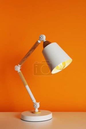 Téléchargez les photos : Stylish modern desk lamp on white table near orange wall - en image libre de droit