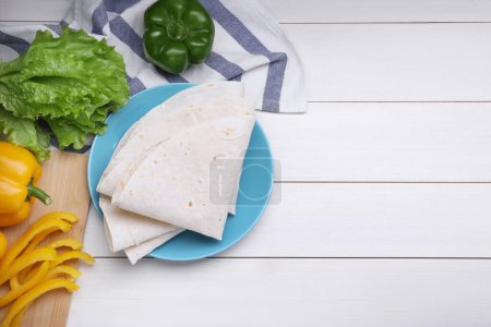 Photo for Delicious folded Armenian lavash and fresh vegetables on white wooden table, flat lay. Space for text - Royalty Free Image
