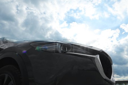 Foto de New black modern car against cloudy sky, closeup of headlight - Imagen libre de derechos