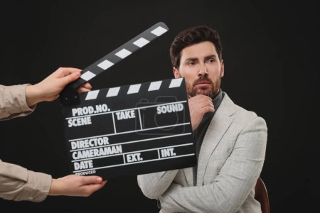 Foto de Actor performing while second assistant camera holding clapperboard on black background - Imagen libre de derechos