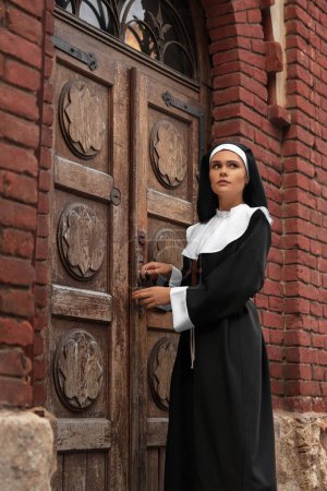 Téléchargez les photos : Young nun near wooden door of old building outdoors - en image libre de droit