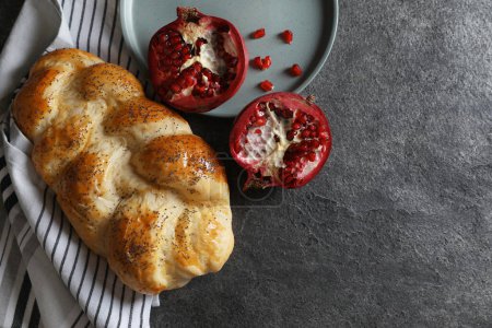 Téléchargez les photos : Homemade braided bread and pomegranate on grey table, flat lay with space for text. Cooking traditional Shabbat challah - en image libre de droit