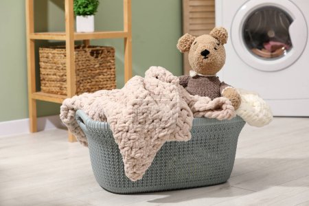 Laundry basket with soft blankets and toy in bathroom