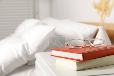 Books and glasses on white wooden bedside table in bedroom, space for text