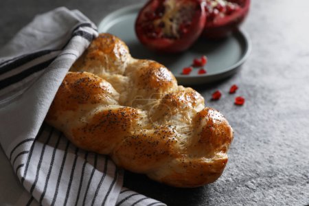 Téléchargez les photos : Homemade braided bread and pomegranate on grey table. Cooking traditional Shabbat challah - en image libre de droit