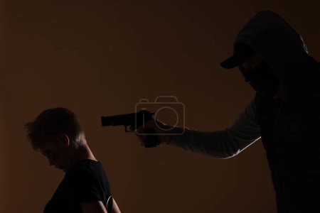 Photo for Kidnapper pointing gun at little boy taken hostage on dark background - Royalty Free Image