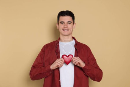 Téléchargez les photos : Happy volunteer holding red heart with hands on beige background - en image libre de droit