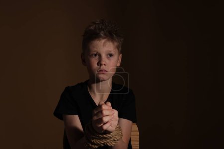Téléchargez les photos : Little boy tied up and taken hostage on dark background - en image libre de droit