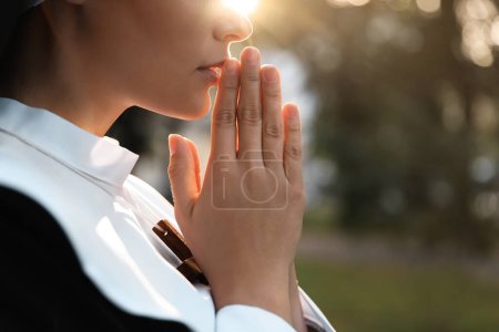 Téléchargez les photos : Young nun with hands clasped together praying outdoors on sunny day, closeup. Space for text - en image libre de droit