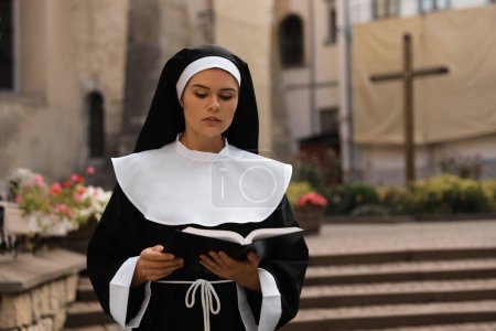 Téléchargez les photos : Young nun reading Bible near building outdoors. Space for text - en image libre de droit
