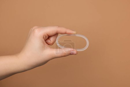 Téléchargez les photos : Woman holding diaphragm vaginal contraceptive ring on light brown background, closeup - en image libre de droit
