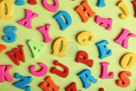 Many colorful magnetic letters on light green background, flat lay