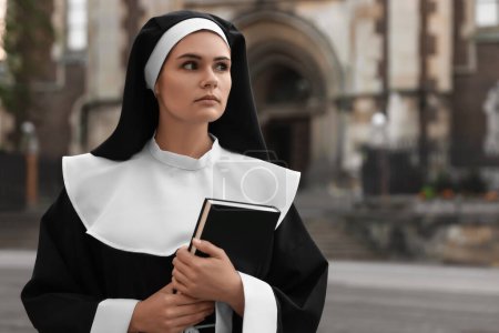 Téléchargez les photos : Young nun with Bible near building outdoors. Space for text - en image libre de droit