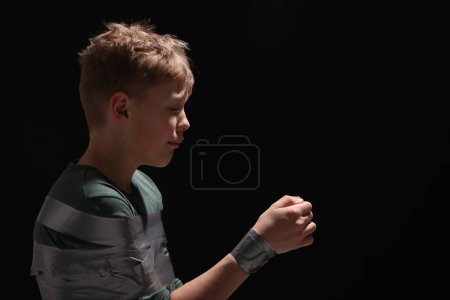 Photo for Little boy tied up and taken hostage on dark background. Space for text - Royalty Free Image