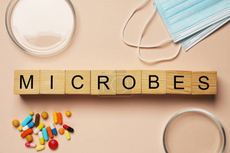 Foto de Word Microbes made with wooden cubes, colorful pills, Petri dishes and face masks on beige background, flat lay - Imagen libre de derechos