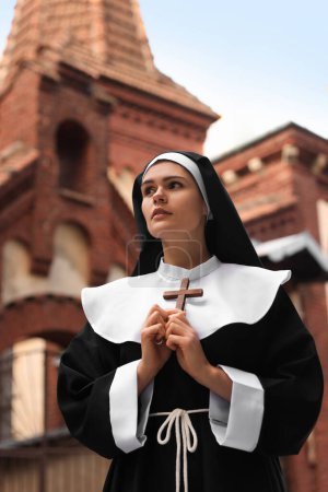 Téléchargez les photos : Young nun holding Christian cross near building outdoors - en image libre de droit