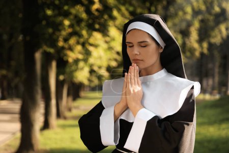 Téléchargez les photos : Young nun with hands clasped together praying in park, space for text - en image libre de droit