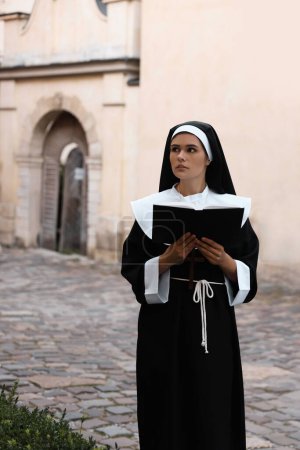 Téléchargez les photos : Young nun reading Bible on city street - en image libre de droit