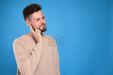 Young man suffering from ear pain on light blue background. Space for text