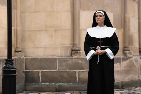 Téléchargez les photos : Young nun with Christian cross near building outdoors. Space for text - en image libre de droit