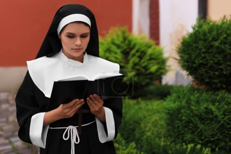 Téléchargez les photos : Young nun reading Bible near building outdoors - en image libre de droit