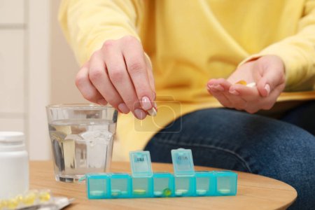 Photo for Woman taking pill from plastic box at wooden table indoors, closeup - Royalty Free Image