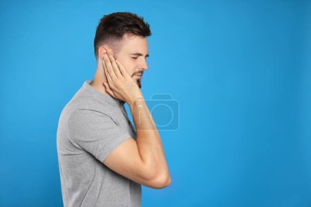 Photo for Young man suffering from ear pain on light blue background. Space for text - Royalty Free Image