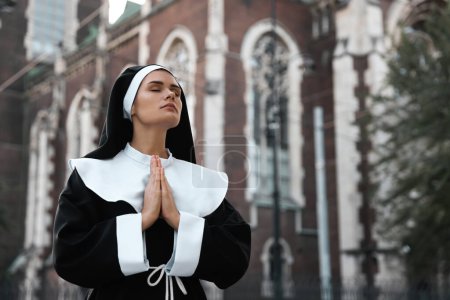 Téléchargez les photos : Jeune religieuse avec les mains jointes tout en priant près de la cathédrale à l'extérieur, espace pour le texte - en image libre de droit