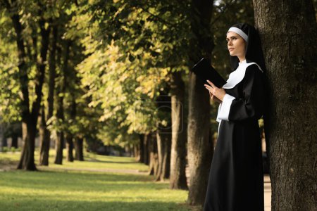 Téléchargez les photos : Jeune religieuse lisant la Bible dans le parc le jour ensoleillé, espace pour le texte - en image libre de droit