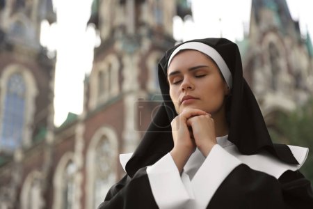 Téléchargez les photos : Jeune religieuse avec les mains jointes tout en priant près de la cathédrale à l'extérieur, espace pour le texte - en image libre de droit