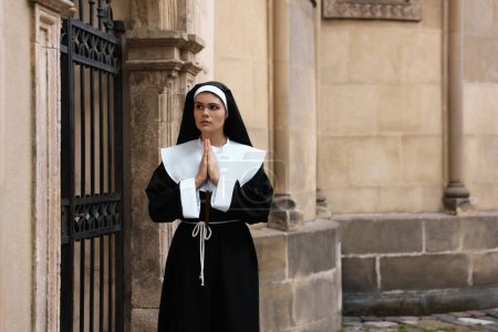 Téléchargez les photos : Young nun with hands clasped together praying near metal door outdoors - en image libre de droit