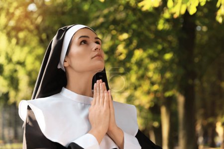 Téléchargez les photos : Young nun with hands clasped together praying in park, space for text - en image libre de droit