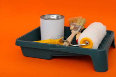 Téléchargez les photos : Can of orange paint, brushes, roller and container on color background - en image libre de droit