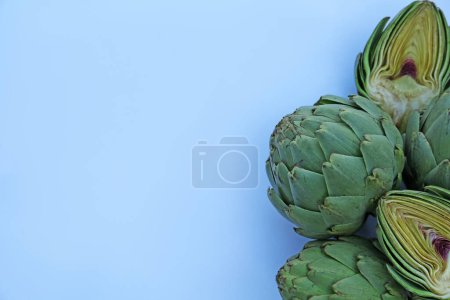Foto de Cut and whole fresh raw artichokes on light blue background, flat lay. Space for text - Imagen libre de derechos