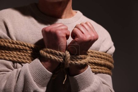 Foto de Victim tied with rope on dark background, closeup. Hostage taking - Imagen libre de derechos