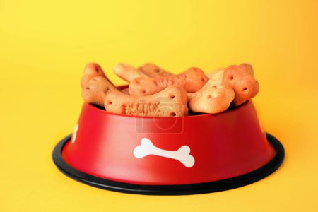 Téléchargez les photos : Bone shaped dog cookies in feeding bowl on yellow background - en image libre de droit