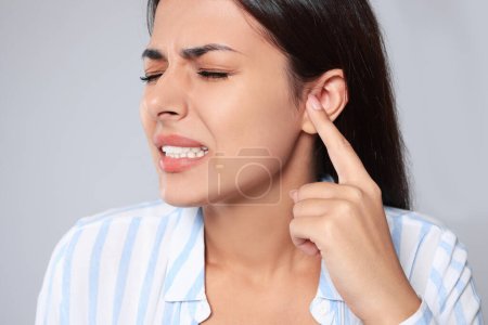 Emotional young woman suffering from ear pain on light grey background, closeup