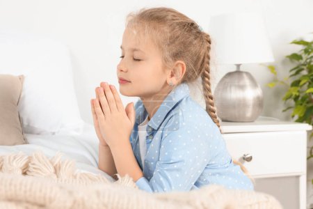 Girl with clasped hands praying near bed at home