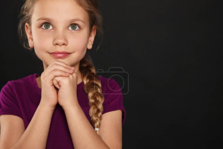 Mädchen mit gefalteten Händen, die auf schwarzem Hintergrund beten, Raum für Text