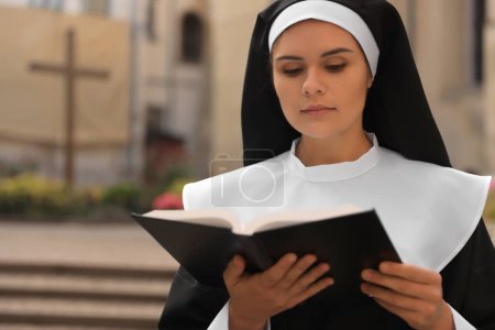Téléchargez les photos : Young nun reading Bible outdoors, space for text - en image libre de droit