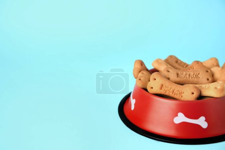 Téléchargez les photos : Bone shaped dog cookies in feeding bowl on light blue background, space for text - en image libre de droit