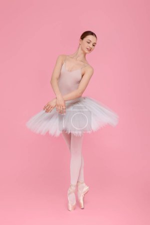 Photo for Young ballerina practicing dance moves on pink background - Royalty Free Image
