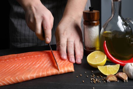 Téléchargez les photos : Man cutting raw salmon at black table, closeup - en image libre de droit