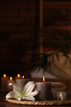 Spa composition with burning candles, lily flower and towels on wooden table in wellness center, space for text