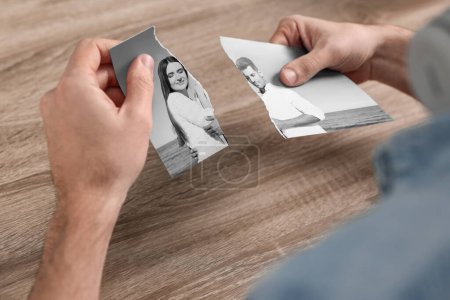 Photo for Divorce and breakup. Man holding parts of ripped black and white photo at table, closeup - Royalty Free Image