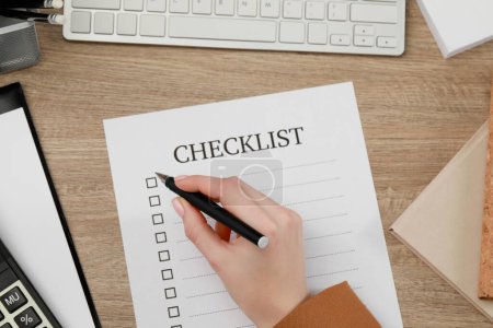 Woman filling Checklist at wooden table, top view