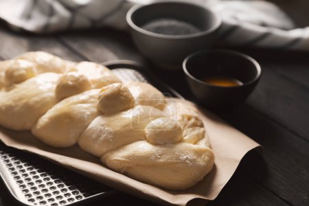 Téléchargez les photos : Raw braided bread and ingredients on black wooden table, closeup. Traditional Shabbat challah - en image libre de droit